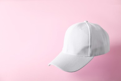 Photo of White baseball hat in air on pink background, space for text