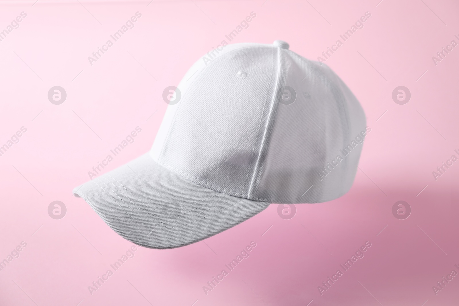White baseball hat in air on pink background Photo of White baseball hat in air on pink background