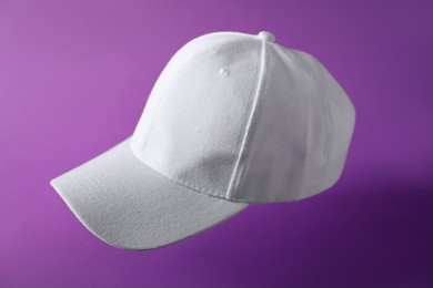 Photo of White baseball hat in air on purple background