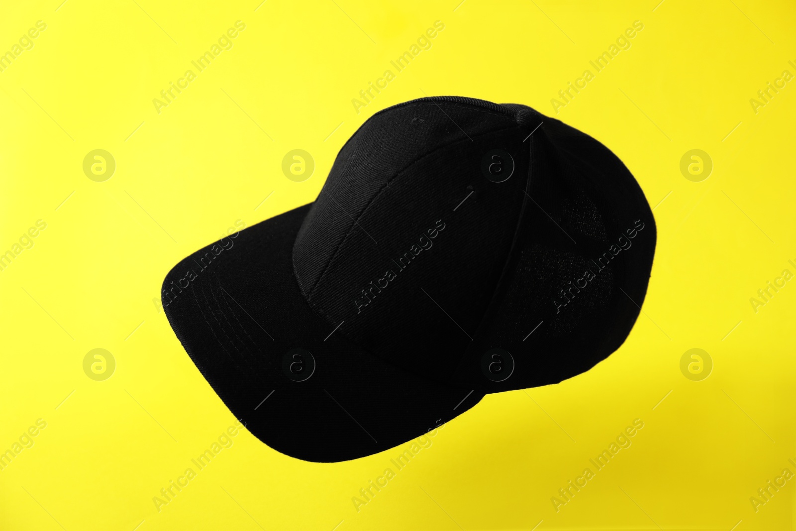 Black baseball hat in air on yellow background Photo of Black baseball hat in air on yellow background