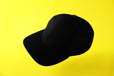 Photo of Black baseball hat in air on yellow background