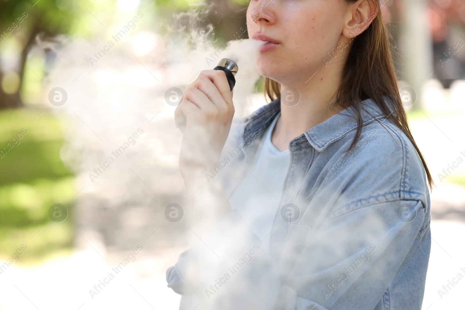 Young woman using electronic smoking device outdoors, closeup. Space for text Photo of Young woman using electronic smoking device outdoors, closeup. Space for text