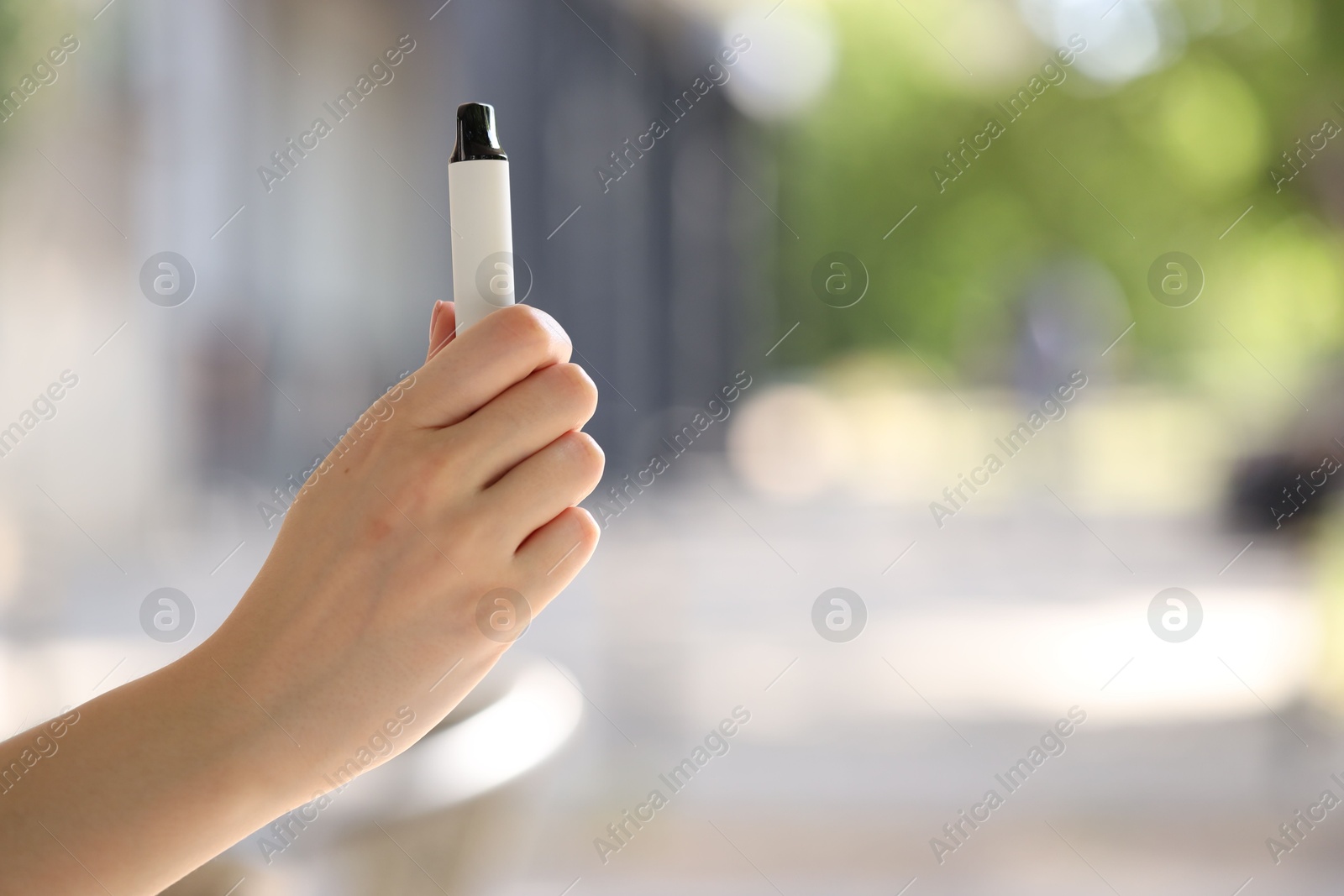 Young woman with electronic smoking device outdoors, closeup. Space for text Photo of Young woman with electronic smoking device outdoors, closeup. Space for text