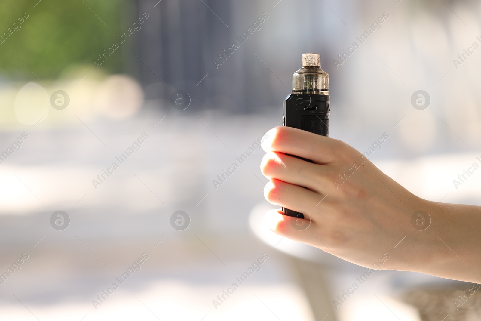 Young woman with electronic smoking device outdoors, closeup. Space for text Photo of Young woman with electronic smoking device outdoors, closeup. Space for text