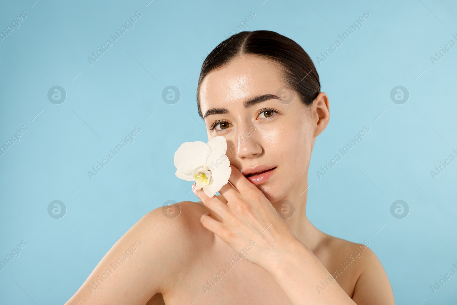Portrait of beautiful woman with orchid flower after spa treatment on light blue background Photo of Portrait of beautiful woman with orchid flower after spa treatment on light blue background