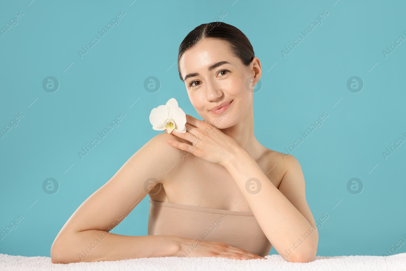 Portrait of beautiful woman with orchid flower and towel after spa treatment on light blue background Photo of Portrait of beautiful woman with orchid flower and towel after spa treatment on light blue background
