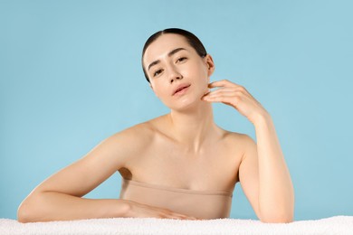 Photo of Portrait of beautiful woman with towel after spa treatment on light blue background