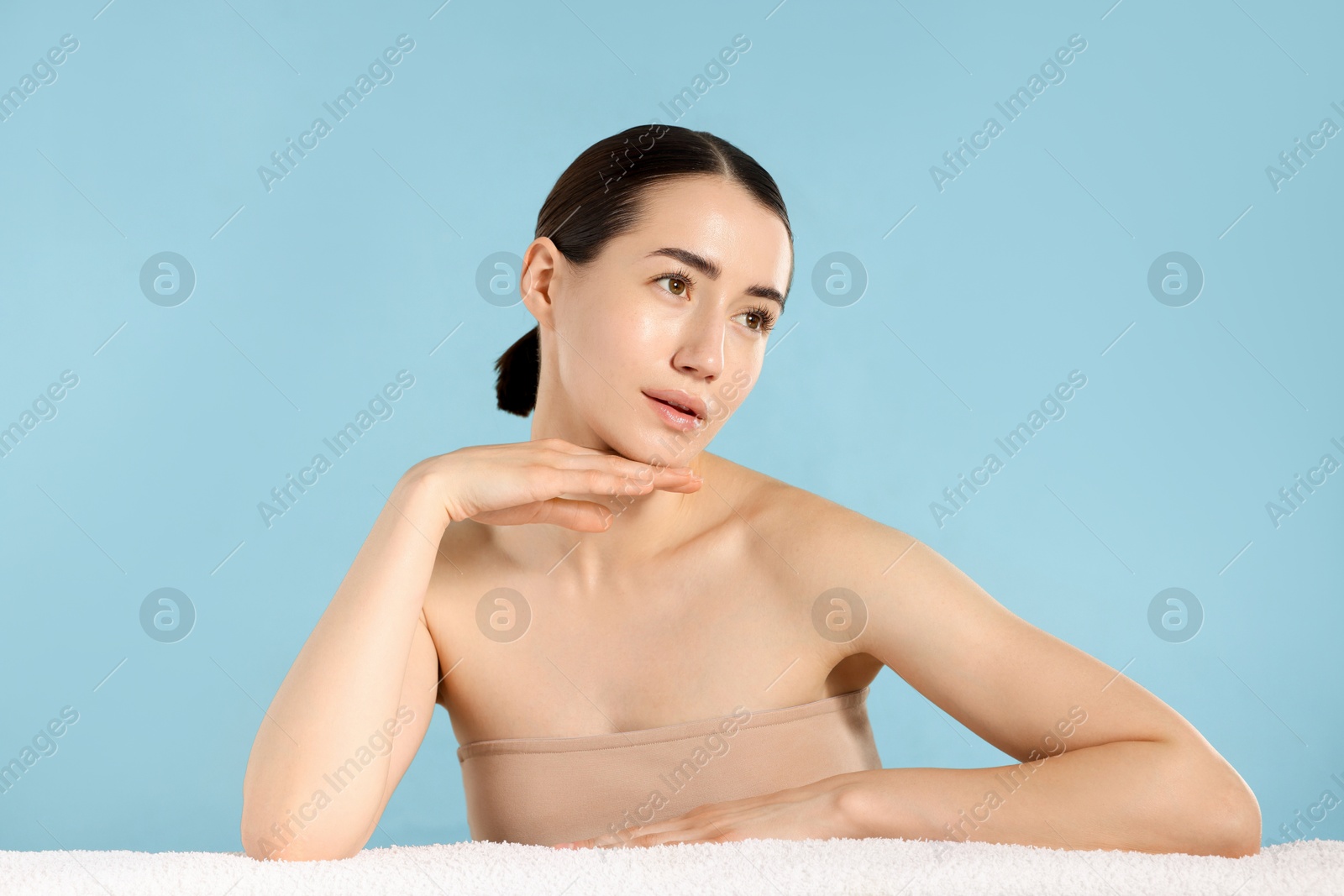 Beautiful woman with towel after spa treatment on light blue background Photo of Beautiful woman with towel after spa treatment on light blue background