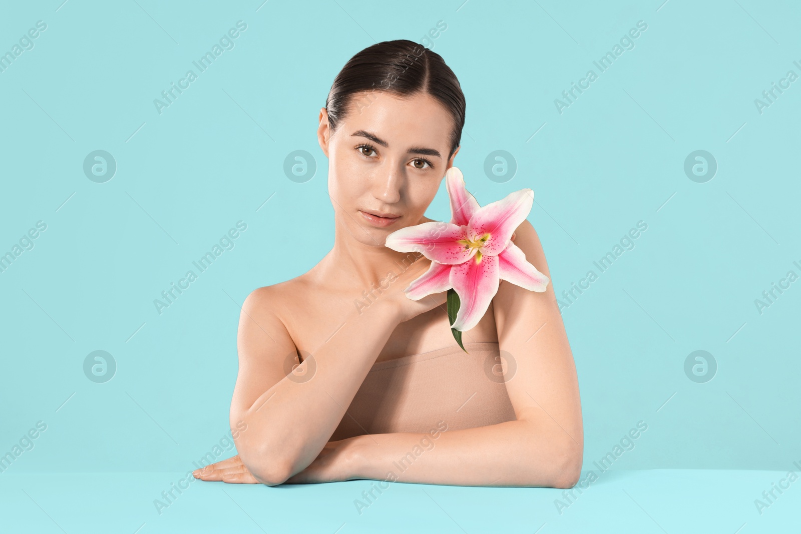 Beautiful woman with lily flower after spa treatment on light blue background Photo of Beautiful woman with lily flower after spa treatment on light blue background