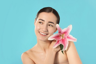 Photo of Smiling woman with lily flower after spa treatment on light blue background