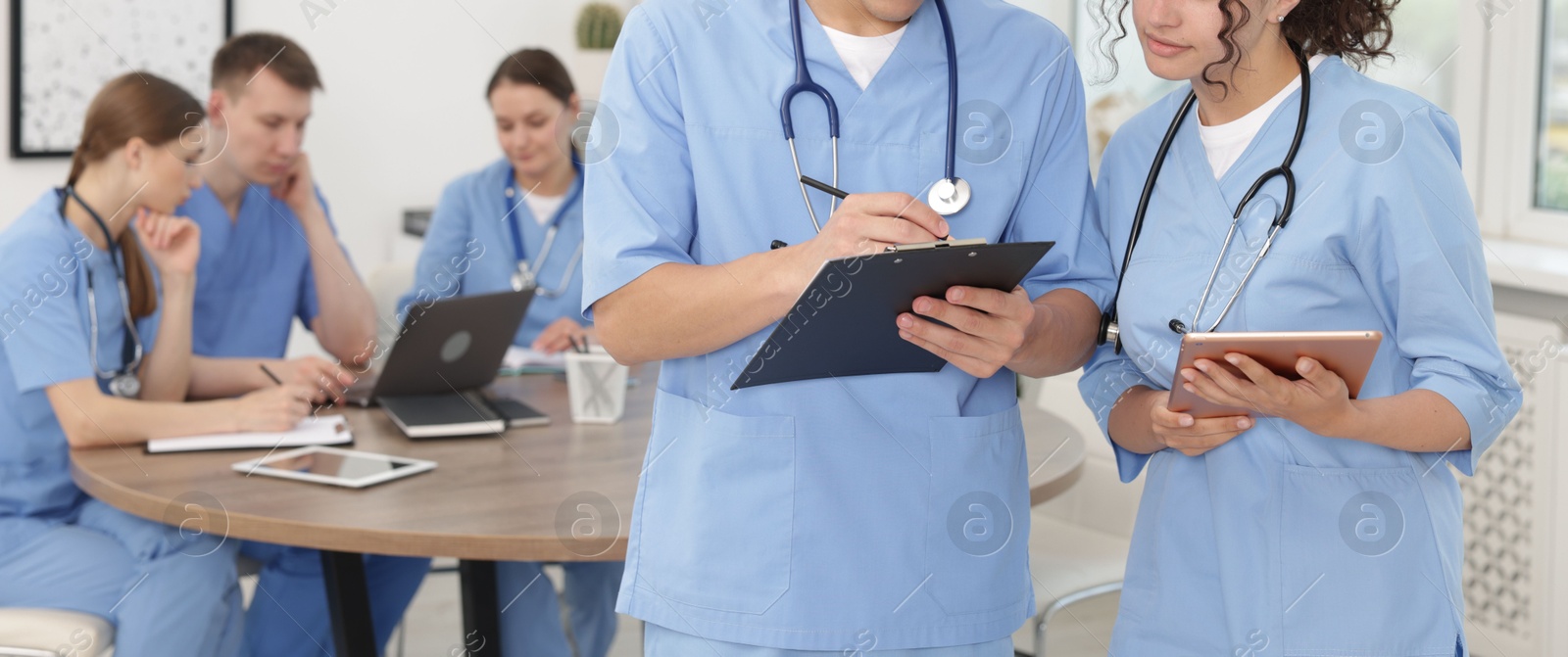 Medical students in uniforms studying together indoors, selective focus Photo of Medical students in uniforms studying together indoors, selective focus