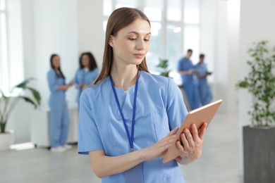 Photo of Medical student in uniform with tablet indoors, selective focus