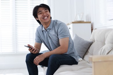 Photo of Smiling Asian man with smartphone on sofa at home