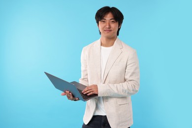 Photo of Handsome Asian businessman in suit with laptop on light blue background
