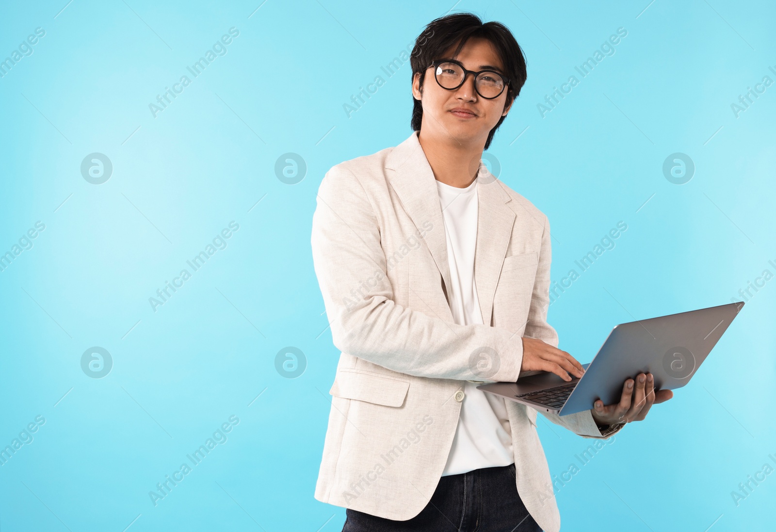 Handsome Asian businessman in glasses with laptop on light blue background Photo of Handsome Asian businessman in glasses with laptop on light blue background