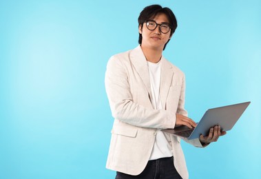 Photo of Handsome Asian businessman in glasses with laptop on light blue background