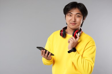 Photo of Handsome Asian man with headphones and smartphone on grey background. Space for text