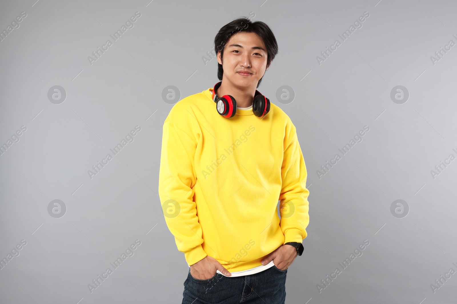 Handsome Asian man with headphones on grey background Photo of Handsome Asian man with headphones on grey background