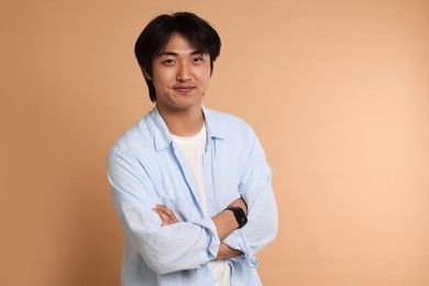 Photo of Portrait of handsome Asian man with crossed arms on beige background