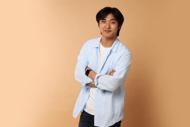 Photo of Portrait of handsome Asian man with crossed arms on beige background. Space for text