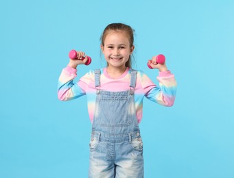 Photo of Little girl with dumbbells on light blue background