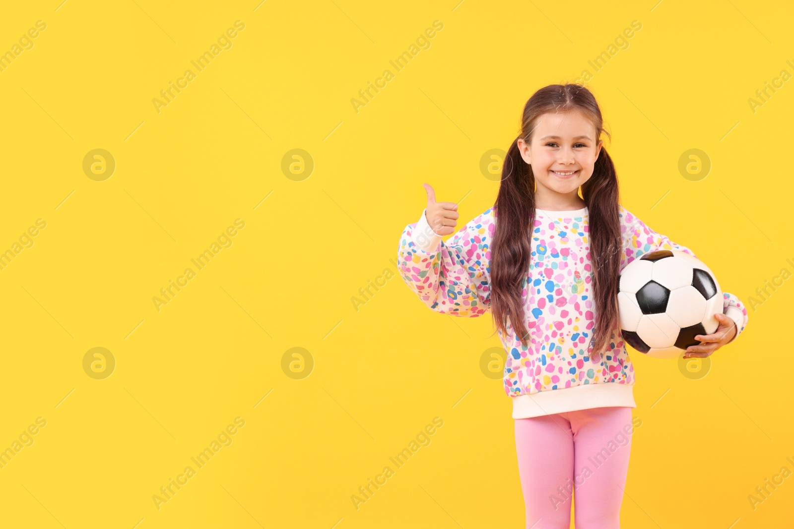 Little girl with soccer ball showing thumbs up on yellow background, space for text Photo of Little girl with soccer ball showing thumbs up on yellow background, space for text