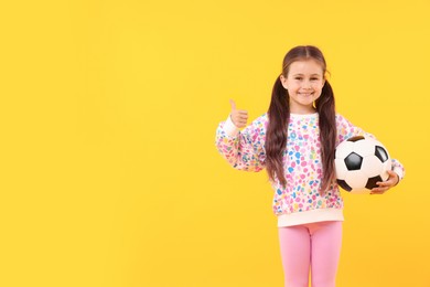 Photo of Little girl with soccer ball showing thumbs up on yellow background, space for text