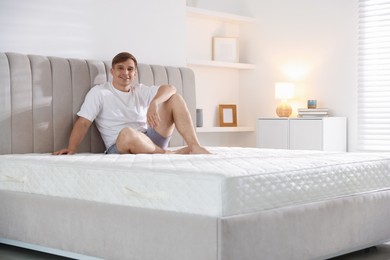 Photo of Young man sitting on bed with soft mattress at home, space for text