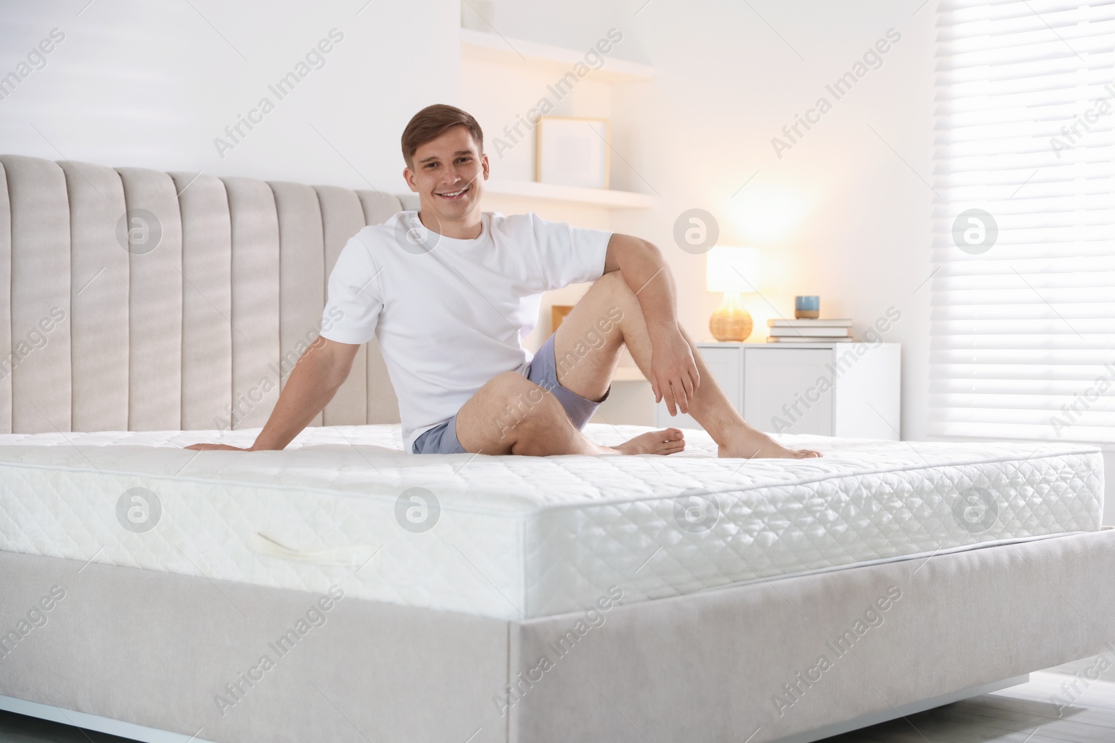 Young man sitting on bed with soft mattress at home Photo of Young man sitting on bed with soft mattress at home