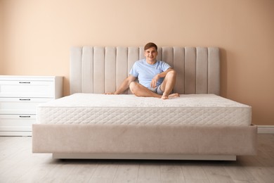 Photo of Young man sitting on bed with soft mattress at home