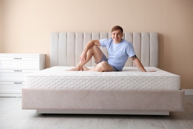 Photo of Young man sitting on bed with soft mattress at home, space for text