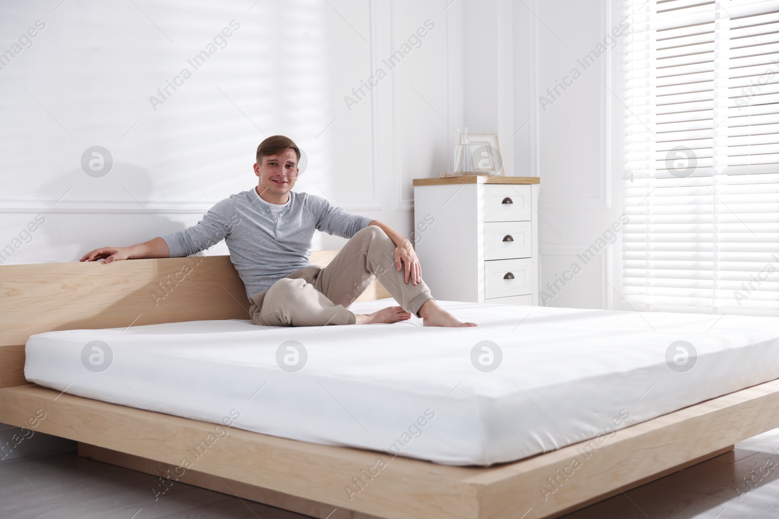 Young man sitting on bed with soft mattress at home, space for text Photo of Young man sitting on bed with soft mattress at home, space for text