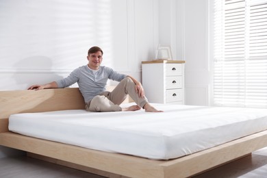 Photo of Young man sitting on bed with soft mattress at home, space for text