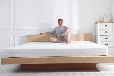 Photo of Young man sitting on bed with soft mattress at home