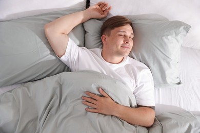 Photo of Young man sleeping on bed with soft mattress at home, top view