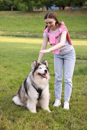 Photo of Smiling woman training her cute Alaskan malamute dog on green grass outdoors