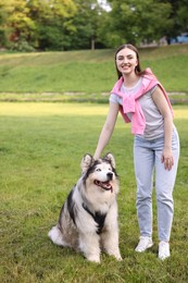 Photo of Smiling woman with her cute Alaskan malamute dog on green grass outdoors