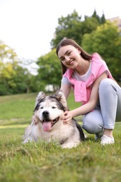 Photo of Smiling woman with her cute Alaskan malamute dog on green grass outdoors