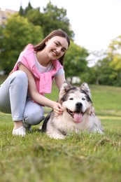 Photo of Smiling woman with her cute Alaskan malamute dog on green grass outdoors
