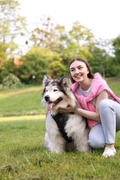 Photo of Smiling woman with her cute Alaskan malamute dog on green grass outdoors