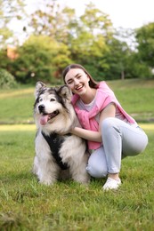 Photo of Smiling woman with her cute Alaskan malamute dog on green grass outdoors
