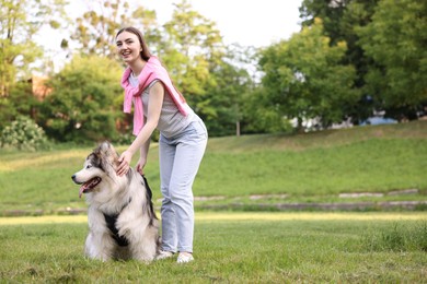 Photo of Smiling woman with her cute Alaskan malamute dog on green grass outdoors. Space for text