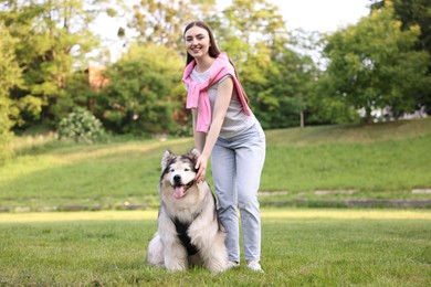 Photo of Smiling woman with her cute Alaskan malamute dog on green grass outdoors