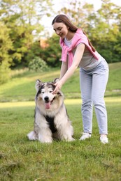 Photo of Smiling woman with her cute Alaskan malamute dog on green grass outdoors