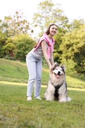 Photo of Smiling woman with her cute Alaskan malamute dog on green grass outdoors, low angle view