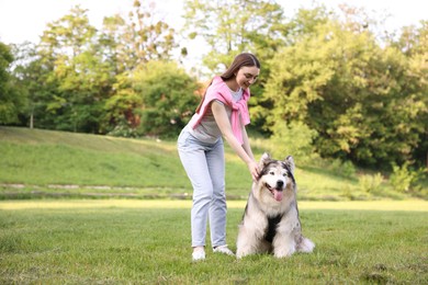 Photo of Smiling woman with her cute Alaskan malamute dog on green grass outdoors