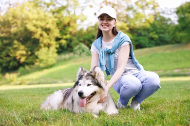 Photo of Smiling woman with her cute Alaskan malamute dog on green grass outdoors