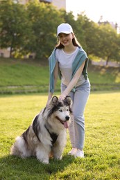 Photo of Smiling woman with her cute Alaskan malamute dog on green grass outdoors in morning