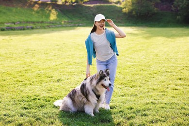 Photo of Smiling woman with her cute Alaskan malamute dog on green grass outdoors in morning