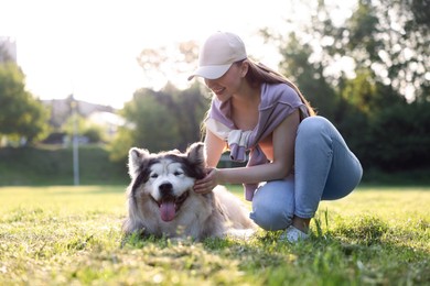 Photo of Smiling woman with her cute Alaskan malamute dog on green grass outdoors in morning